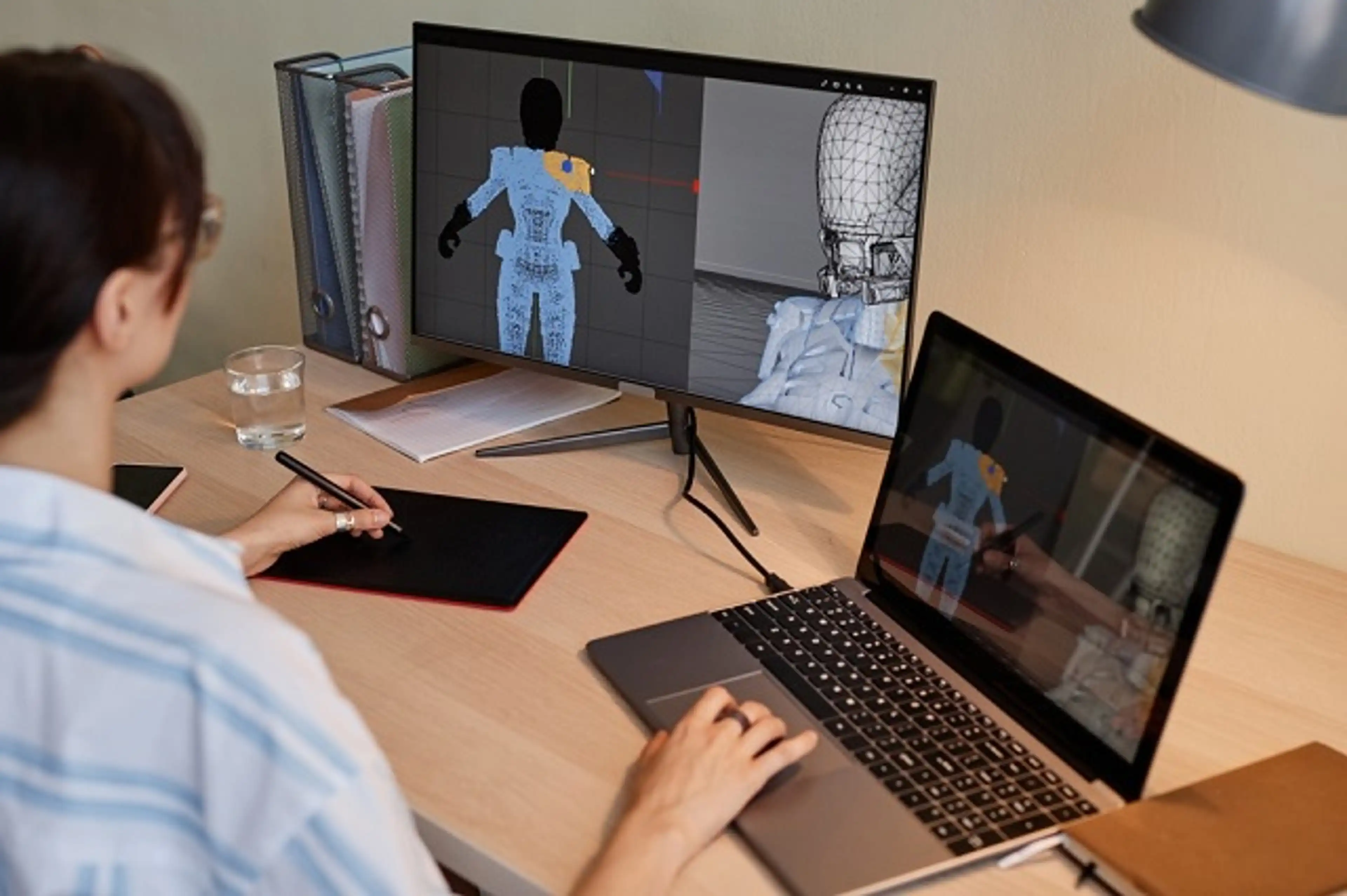 Young female designer building digital 3D models for videogame characters at workplace and using pen tablet