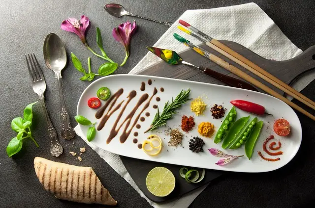 Colorful ingredients arranged artistically on a plate with herbs, spices, and sauces, symbolizing creativity and presentation in culinary art.