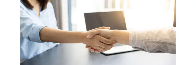 Handshake between a man and woman over a desk in front of a laptop
