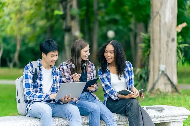 Three students doing group work on a bench in campus