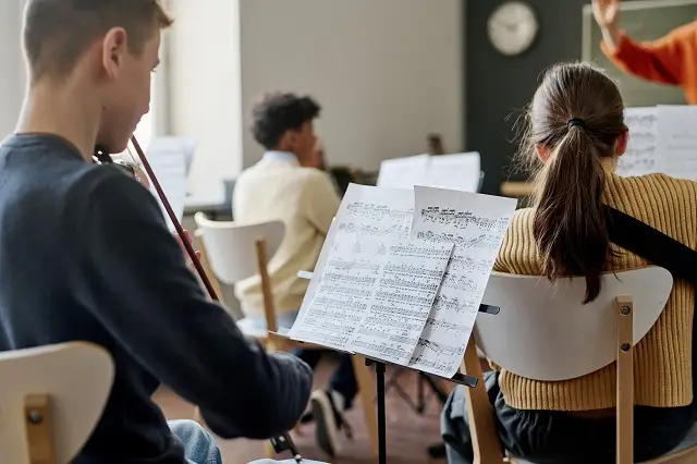 Selective focus shot of group of teenagers playing instrumental music in school orchestra at class