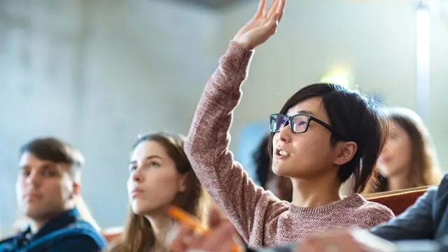 Image of multiple students sitting in classroom style with one raising hand