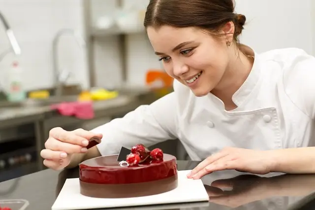 Student carefully decorating a glossy chocolate cake with cherries, demonstrating creativity and precision in culinary art.