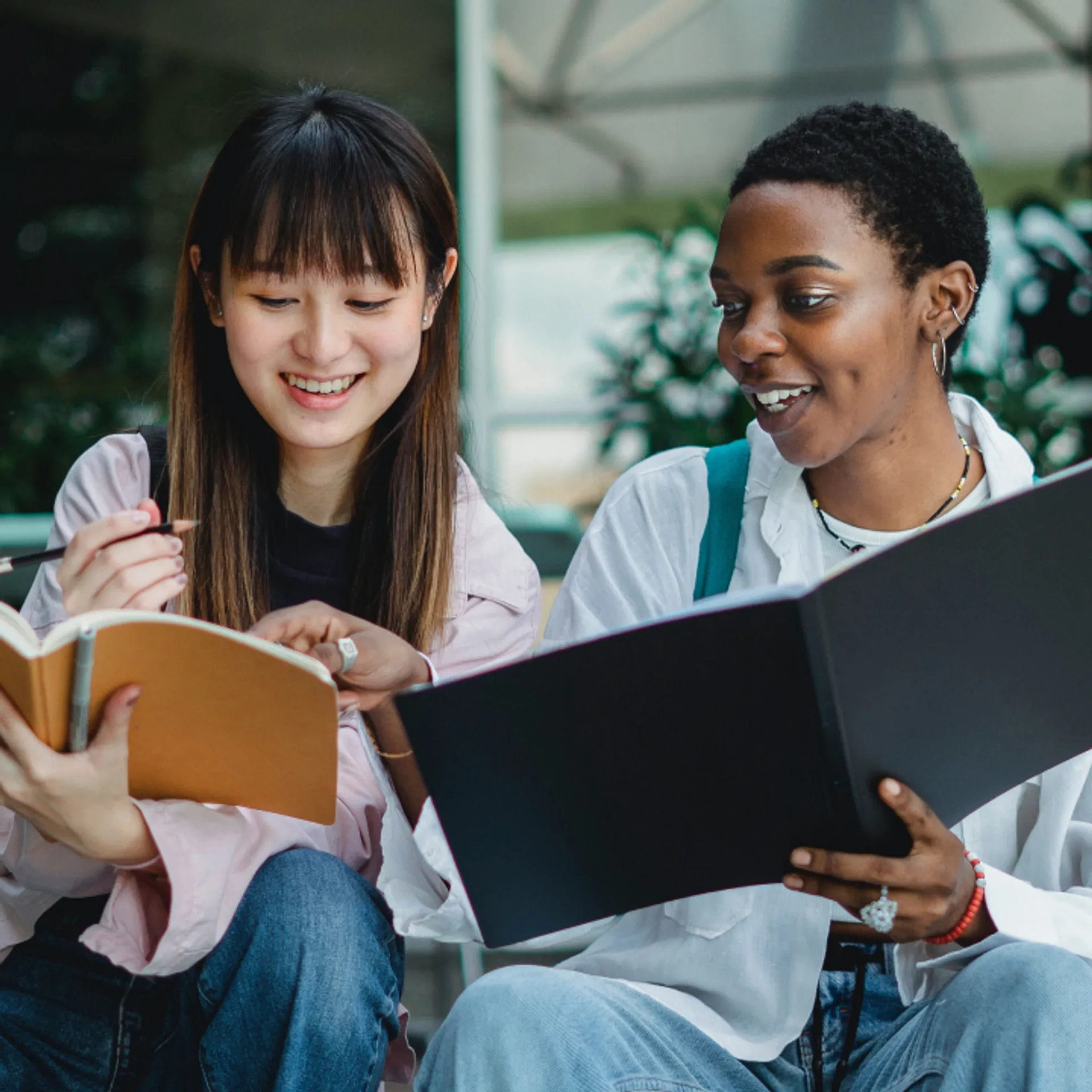 One girl explains to the other pointing to her notebook